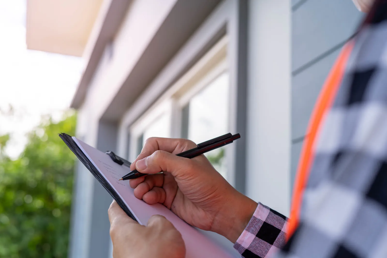 An inspector making notes on a clipboard beside a house