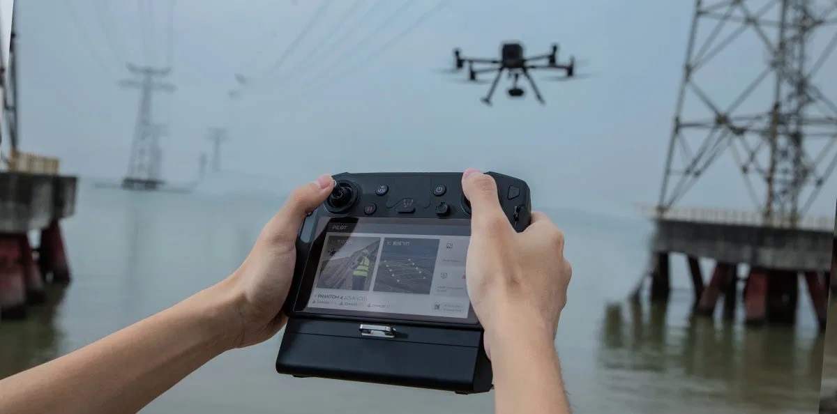 Hands operating a drone controller, the aircraft in flight above
